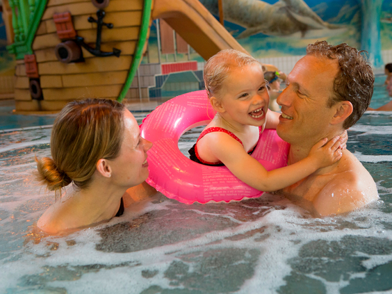 Een gezin met een klein kind in een zwemband geniet in het warme bubbelbad van het zwembad op Landal Coldenhove.
