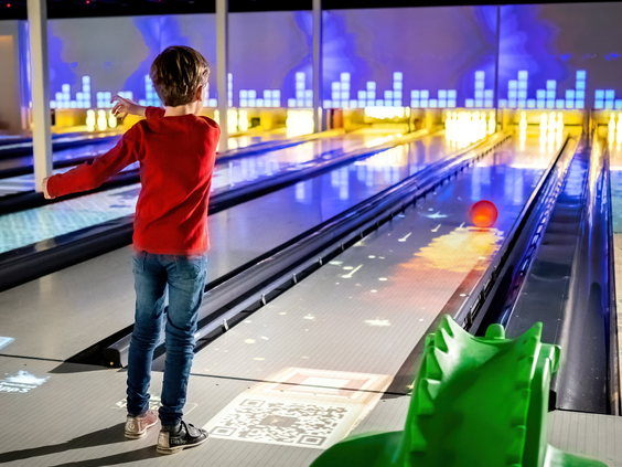 Kind gooit een bowlingbal op de hypermoderne, interactieve bowlingbaan met lichteffecten en een dinosaurus-hulpje op vakantiepark Landal De Lommerbergen.