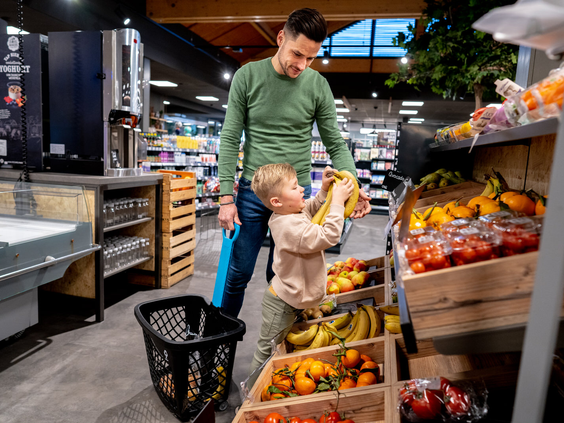 Vader en zoon doen samen boodschappen in de parkwinkel van Landal De Lommerbergen en kiezen vers fruit uit voor het ontbijt.