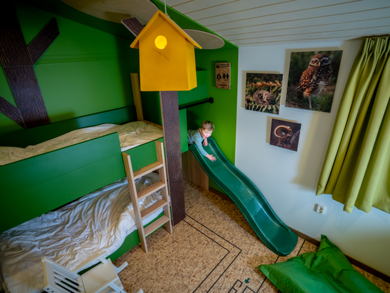 De avontuurlijke kinderslaapkamer in een speciale kinderbungalow op Landal De Lommerbergen, met een boomhut-stapelbed en een eigen glijbaan.