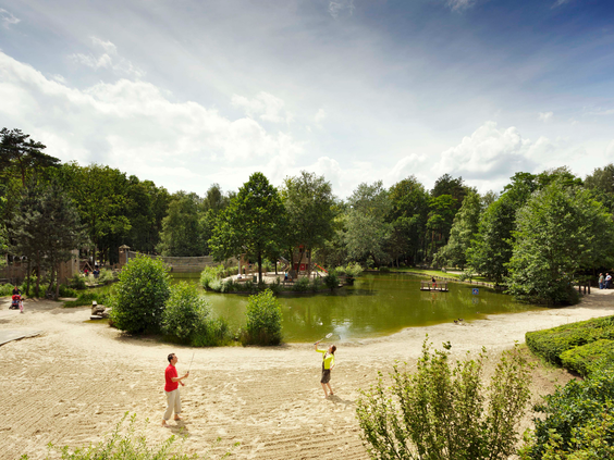 Kinderen spelen aan de rand van de grote speelvijver met zandstrand, omgeven door bomen, op het bosrijke vakantiepark Landal De Lommerbergen in Limburg.