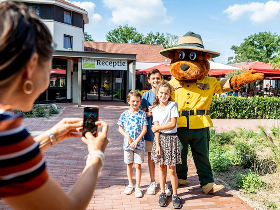 Moeder maakt een foto van haar kinderen die poseren met Bollo de beer bij de ingang van Landal De Vers.