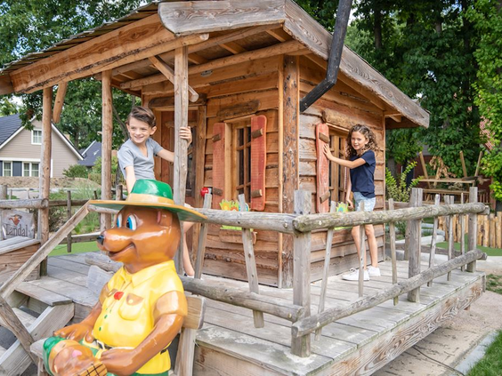 Kinderen spelen bij het houten speelhuisje van Bollo, met een standbeeld van de mascotte ervoor.