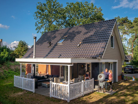 Vrijstaande bungalow op Landal De Vers met een ruim, overdekt terras waar een gezin aan het barbecueën is.
