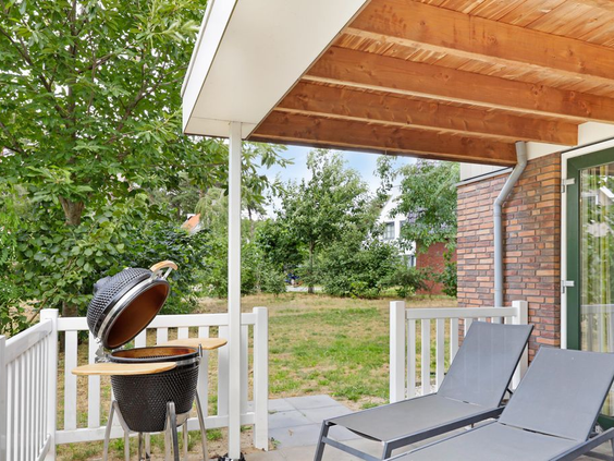 Het overdekte terras van een bungalow op Landal de Vers, uitgerust met een barbecue en comfortabele ligbedden.