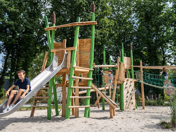 Grote houten natuurspeeltuin met glijbaan, klimwand en touwbrug in het zand op Landal De Vers.