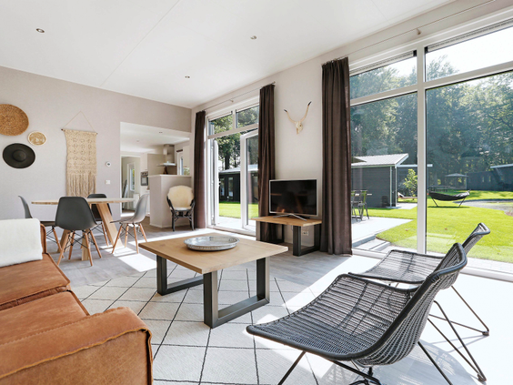 De lichte, moderne woonkamer van een lodge op Landal De Vlinderhoeve met grote ramen en openslaande deuren naar de tuin.