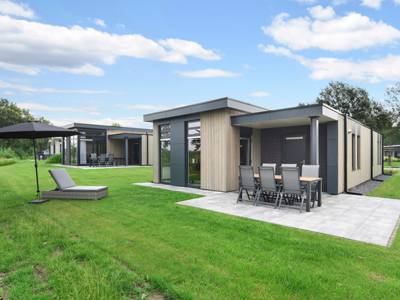 De buitenkant van een vrijstaande, moderne bungalow op Landal De Vlinderhoeve met een gemeubileerd terras en een groot groen grasveld.