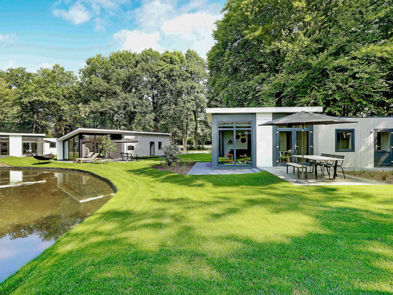 Moderne bungalows van Landal De Vlinderhoeve, gelegen aan een grote vijver omringd door bomen en een groen gazon.