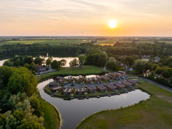 Een prachtige luchtfoto van Landal De Wedderplassen tijdens zonsondergang, waarbij de vakantiehuizen mooi oplichten aan het water.
