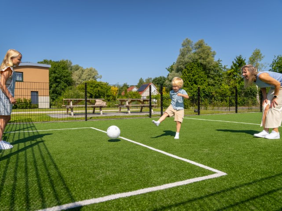 Een gezin, bestaande uit een moeder en twee kinderen, speelt enthousiast voetbal op het multifunctionele sportveld van Landal De Wedderplassen.