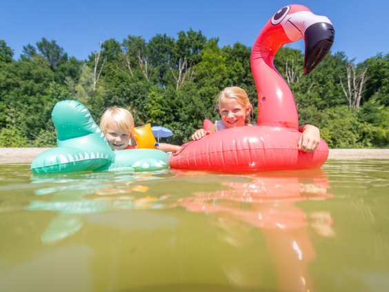 Twee blije kinderen dobberen op een grote opblaasbare roze flamingo in het recreatiemeer van Landal De Wedderplassen.