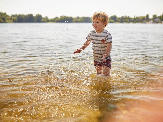 Een klein jongetje speelt en spettert in het ondiepe water van de Wedderplassen bij Landal.