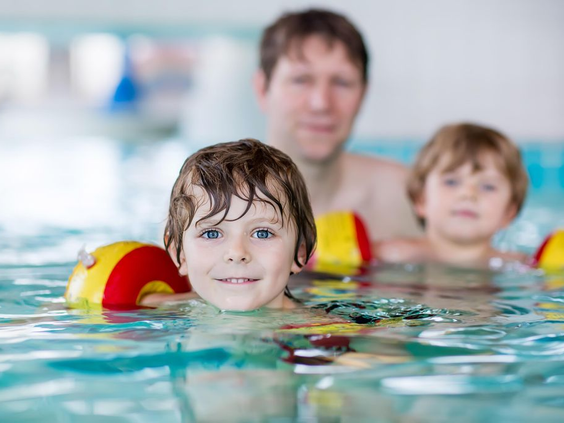 Een vader met zijn twee jonge kinderen, die zwemvleugels dragen, in het binnenzwembad van Landal De Wedderplassen.