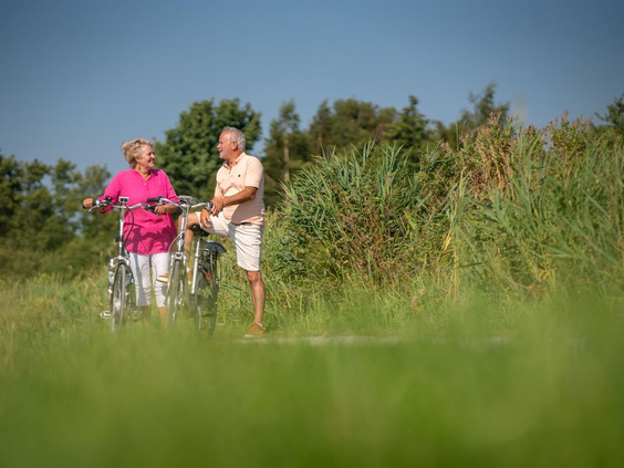Opa en oma maken een wandeling met de fiets door het groene, natuurrijke landschap in de omgeving van Landal De Wedderplassen.