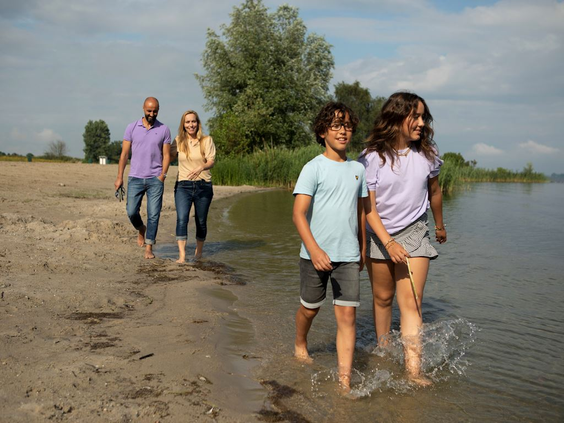 Een gezin wandelt langs de waterkant van het recreatiemeer bij Landal Drentse Lagune, terwijl de kinderen door het ondiepe water waden.