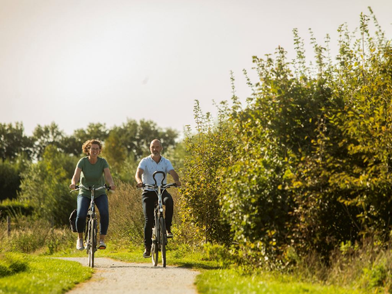Een stel fietst over een zandpad door de groene, bosrijke natuur in de omgeving van vakantiepark Landal Drentse Lagune.