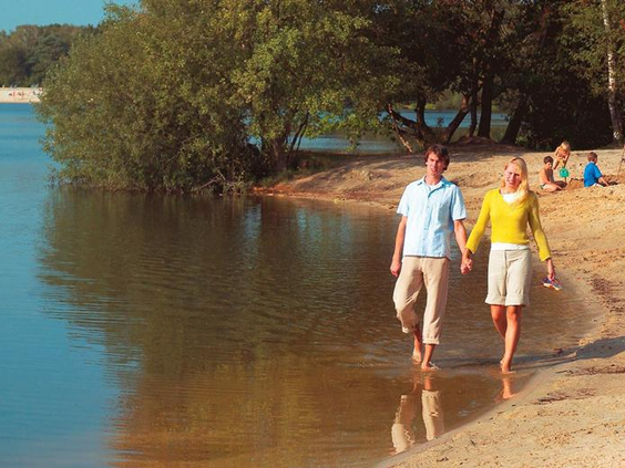 Een stel wandelt hand in hand langs de waterkant van het recreatiemeer met zandstrand, gelegen naast Landal Dwergter Sand.