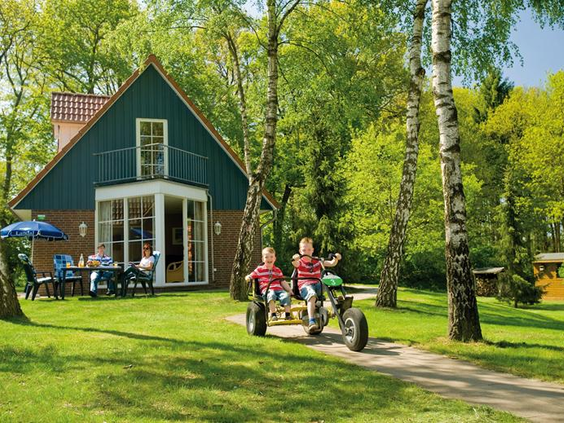 Twee kinderen rijden op een dubbele skelter over het grasveld bij hun vakantiehuisje op Landal Dwergter Sand.