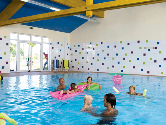 Kinderen en een baby spetteren en spelen vrolijk met speelmatten in het overdekte zwembad van Landal Dwergter Sand.