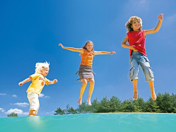 Drie blije kinderen springen zo hoog als ze kunnen op de grote airtrampoline van Landal Dwergter Sand.