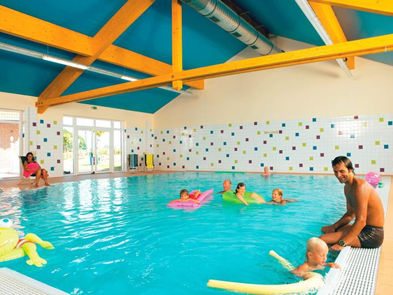 Kinderen en volwassenen vermaken zich in het overdekte zwembad van Landal Dwergter Sand, dobberend op kleurrijke matten.