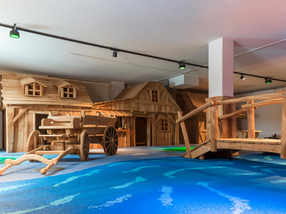Overzicht van het grote houten binnenspeelparadijs van Landal Eifeler Tor, met klimstructuren, een boerderijthema en een zachte speelvloer.