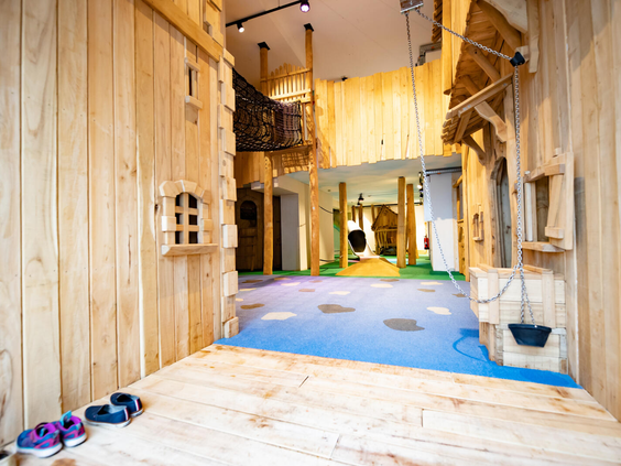 De ingang van het houten indoorspeelparadijs op Landal Eifeler Tor, waar kinderen op een zachte vloer tussen de houten speelhuisjes kunnen spelen.