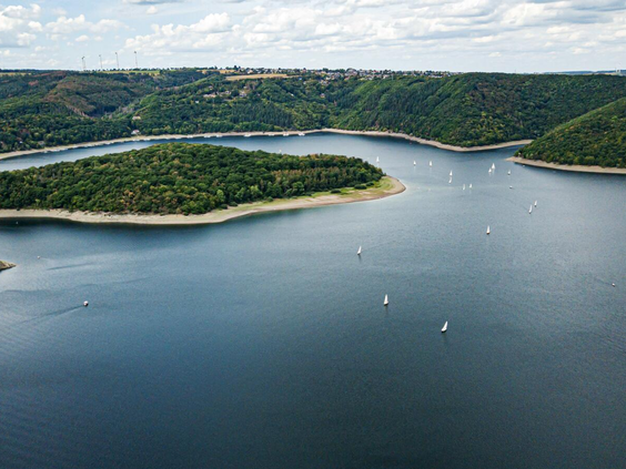 Uitzicht op het stuwmeer de Rursee, direct gelegen bij Landal Eifeler Tor, met zeilbootjes op het water in de heuvelachtige omgeving van de Eifel.