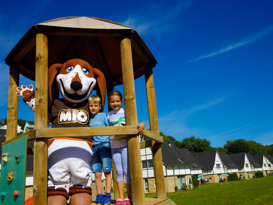 Mascotte Bollo de Beer kijkt samen met twee kinderen vanuit een houten speeltoren in de buitenspeeltuin van Landal Eifeler Tor.