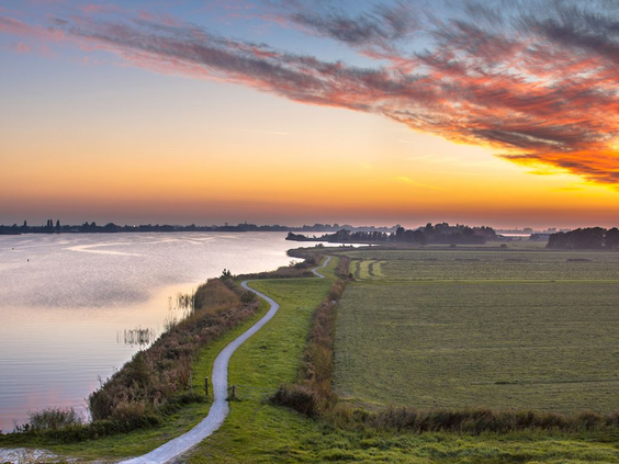 Adembenemende zonsondergang met een oranje en roze lucht boven het water en de weilanden in de omgeving van Landal Elfstedenhart.