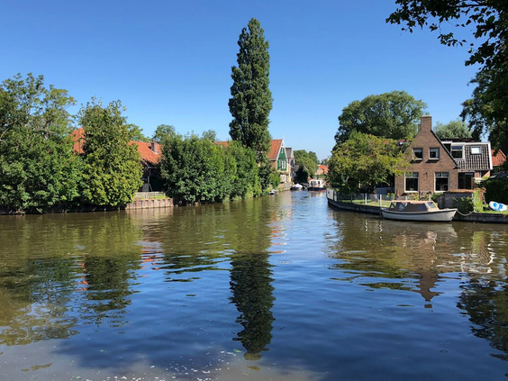 Zonnig beeld van een van de idyllische Elfsteden-stadjes in Friesland, met bootjes en historische huizen langs de gracht.
