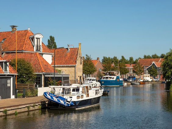 Een sfeervol Fries dorpje met karakteristieke huizen en woonboten die liggen aangemeerd in de gracht op een zonnige middag.