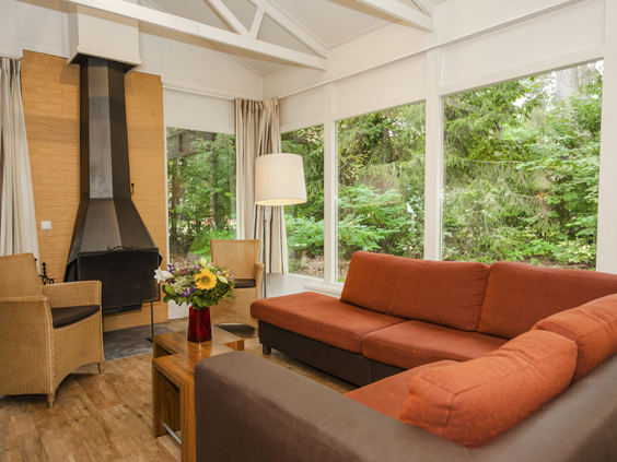Een comfortabele zithoek met open haard in een bungalow op Landal Heideheuvel, met grote ramen die uitkijken op het omliggende bos.