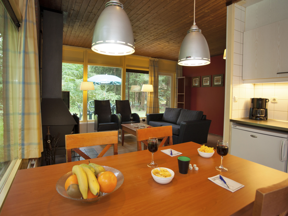 De eethoek in een bungalow op Landal Heideheuvel met een houten tafel, een schaal fruit en uitzicht op de zithoek en het terras.
