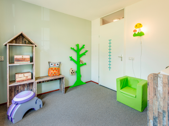 Een vrolijke speelhoek in een kinderkamer van een bungalow, met een kinderstoeltje, een groeimeter en een kapstok in de vorm van een boom.