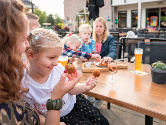 Een gezin geniet van een hapje en een drankje op het zonnige terras van het parkrestaurant op Landal Hellendoornse Berg.
