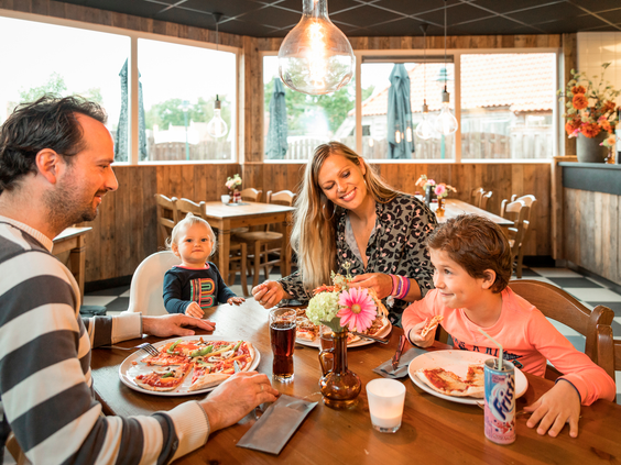 Een gezin met kinderen eet gezellig samen pizza's aan een tafel in het restaurant van Landal Hellendoornse Berg.