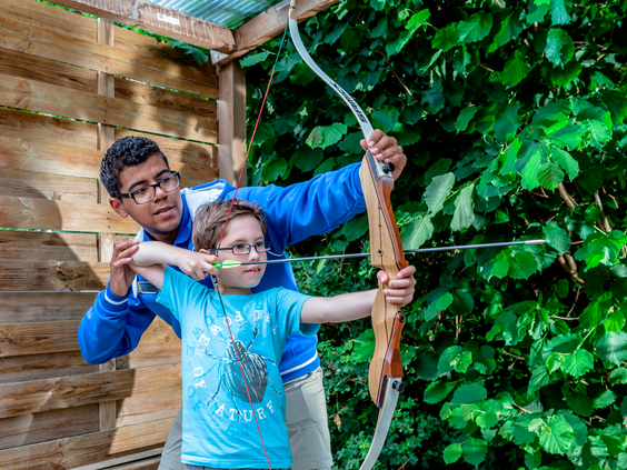 Een jongen leert boogschieten onder begeleiding van een instructeur tijdens de activiteiten van het Fun & Entertainment team.