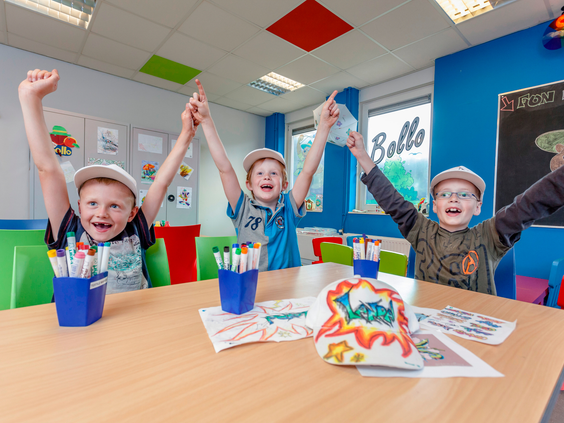 Drie enthousiaste jongens juichen aan een tafel vol knutselspullen in de Bollo Club op Landal Hellendoornse Berg.