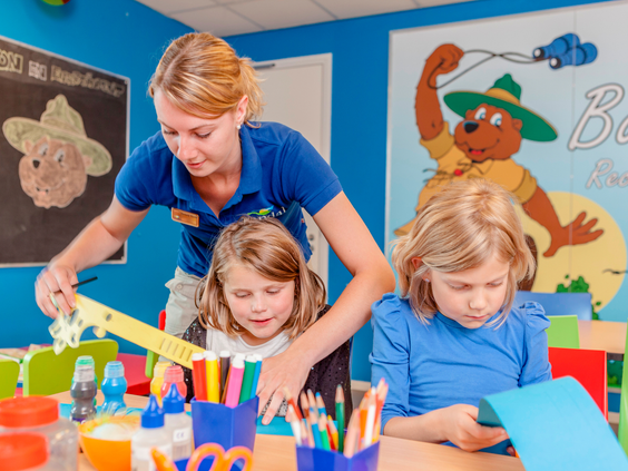 Twee meisjes zijn geconcentreerd aan het knutselen onder begeleiding van een medewerker van het Fun & Entertainment team.