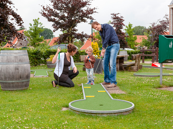 Een gezin met een jong kind speelt samen midgetgolf op de midgetgolfbaan van Landal Hellendoornse Berg.