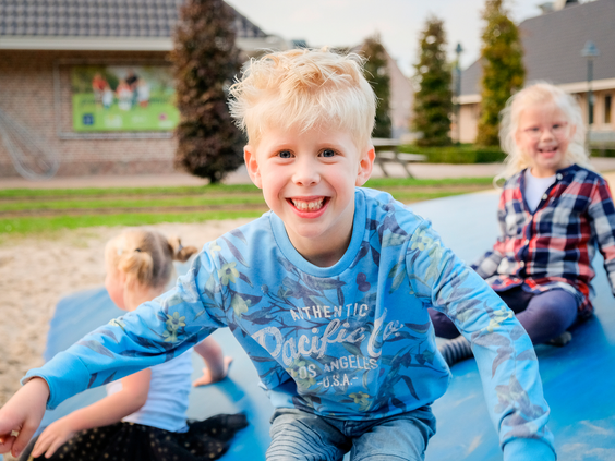 Een lachende, blonde jongen glijdt van een groot luchtkussen in de buitenspeeltuin van Landal Hellendoornse Berg.