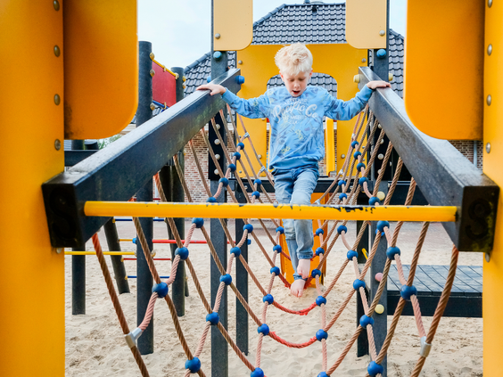 Een jongen balanceert behendig over een touwbrug in het avontuurlijke klimparcours van de buitenspeeltuin.
