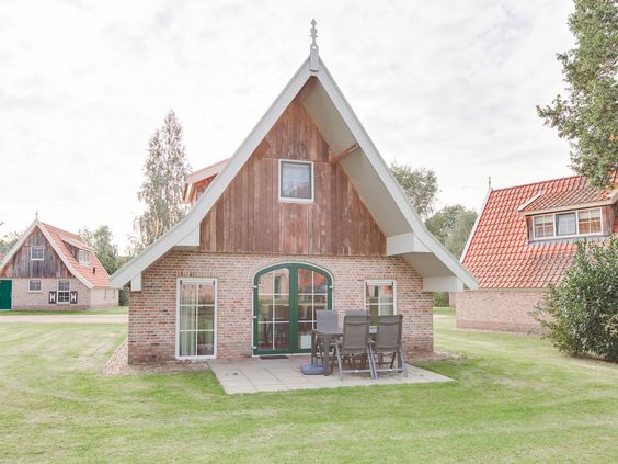 De voorkant van een vrijstaande, sfeervolle bungalow in Twentse boerderijstijl met een terras op een groot grasveld.