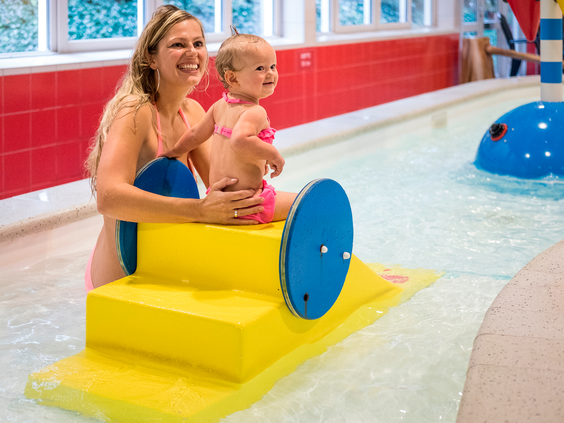 Een moeder zit met haar baby in het ondiepe, warme water van het speciaal ingerichte kinder-doe-bad in het zwembad.