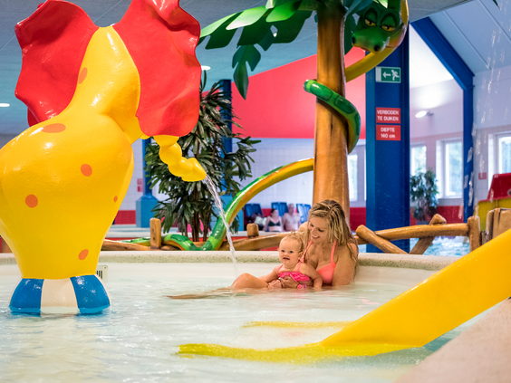 Een moeder speelt met haar dochter in het vrolijke kinderbad, dat is uitgerust met een spuitende olifant en andere speeltoestellen.