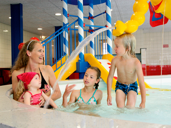 Een moeder geniet samen met haar drie kinderen van het water in het vrolijk aangeklede kinderbad van het zwembad.