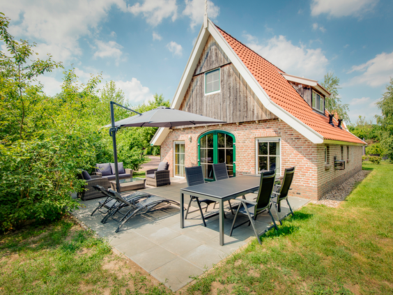 Een ruim, gemeubileerd terras met loungeset, eettafel en parasol bij een vrijstaande bungalow midden in het groen op Landal Hellendoornse Berg.