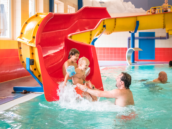 Een vader vangt zijn twee kinderen op die met een grote plons van de brede waterglijbaan het zwembad in komen.